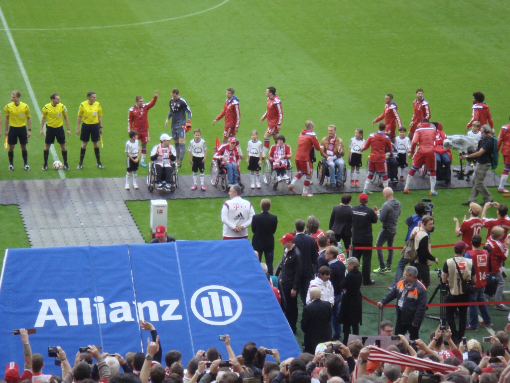 Einige Fußballspieler geben den Rollifahrern die Hand, andere stellen sich hinter ihnen in einer Reihe auf