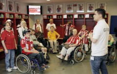 Ein Mann steht mit einer Gruppe Rollstuhlfahrer*innen in der Mannschaftskabine des FC Bayern