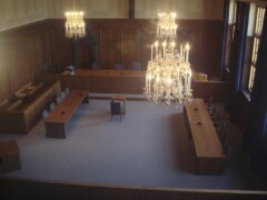 Ein alter Gerichtssaal mit Kronleuchtern an der Decke und aus dunklem Holz vertafelten Wänden und Sitzreihen