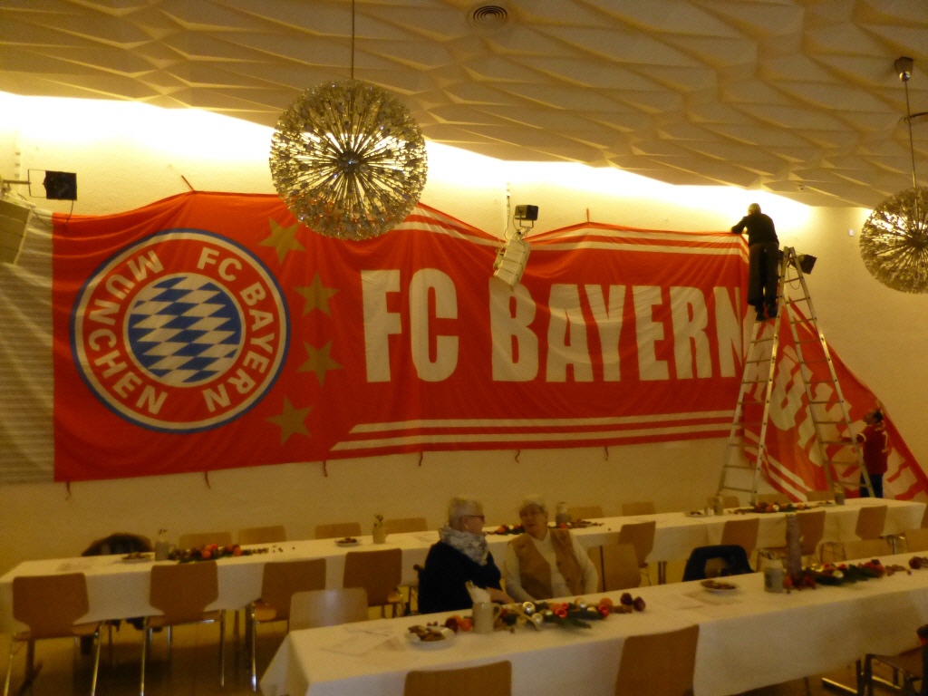 Zwei Männer hängen ein großes Bayern Banner an der Wand auf