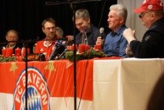 Erwin, Kim, Jupp und Uli sitzen hinter einem Tisch mit Bayern Logo, einer spricht ins Mikrofon