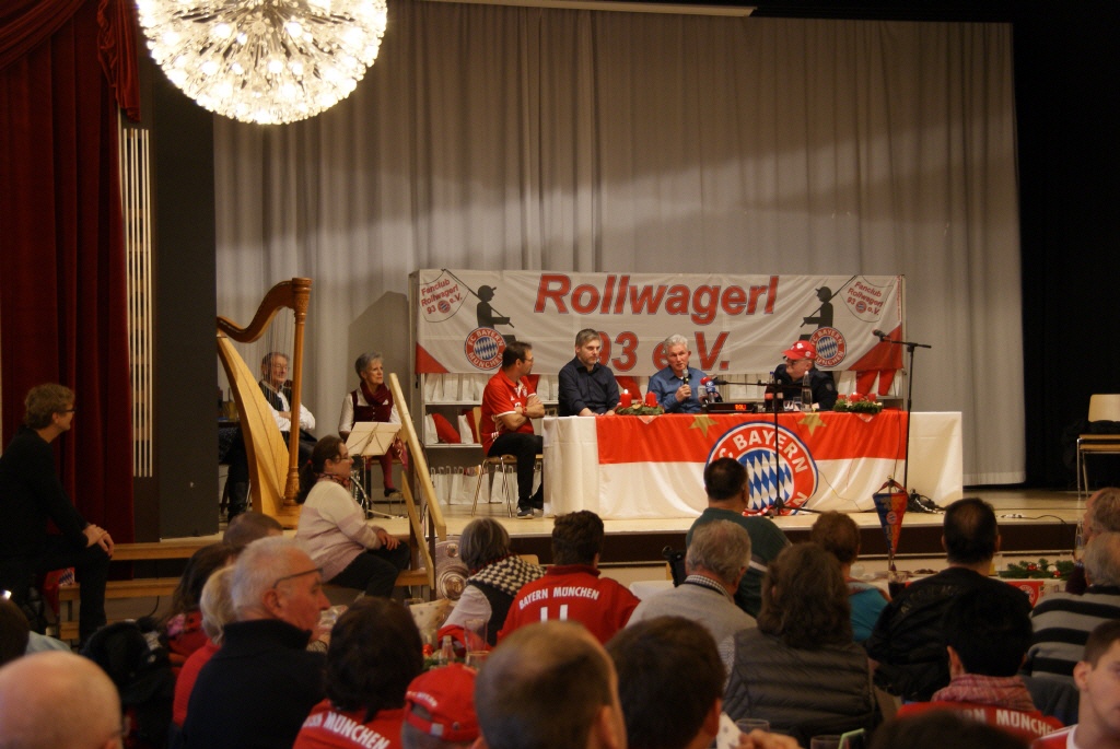 Erwin, Kim, Jupp und Uli sitzen nebeneinander auf der Bühne hinter einem Tisch mit Bayern Logo