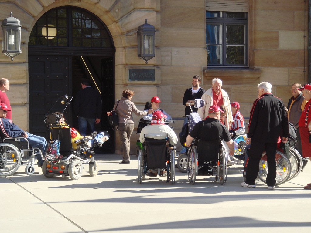 Eine Gruppe aus Rollifahrer*innen und Fußgänger*innen vor einem Gebäude