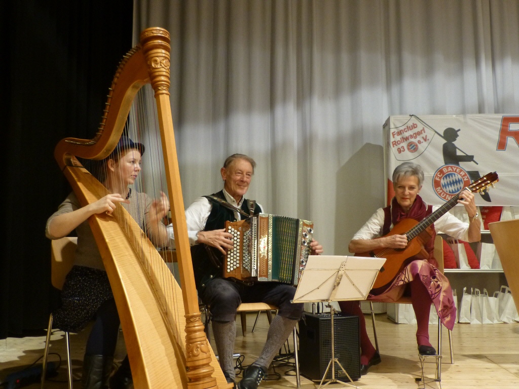 Eine Frau spielt Harfe, eine Gitarre und ein Mann spielt Ziehharmonika auf der Bühne