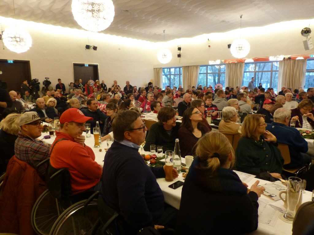 Viele Personen sitzen an langen Tischen und blicken zur Bühne