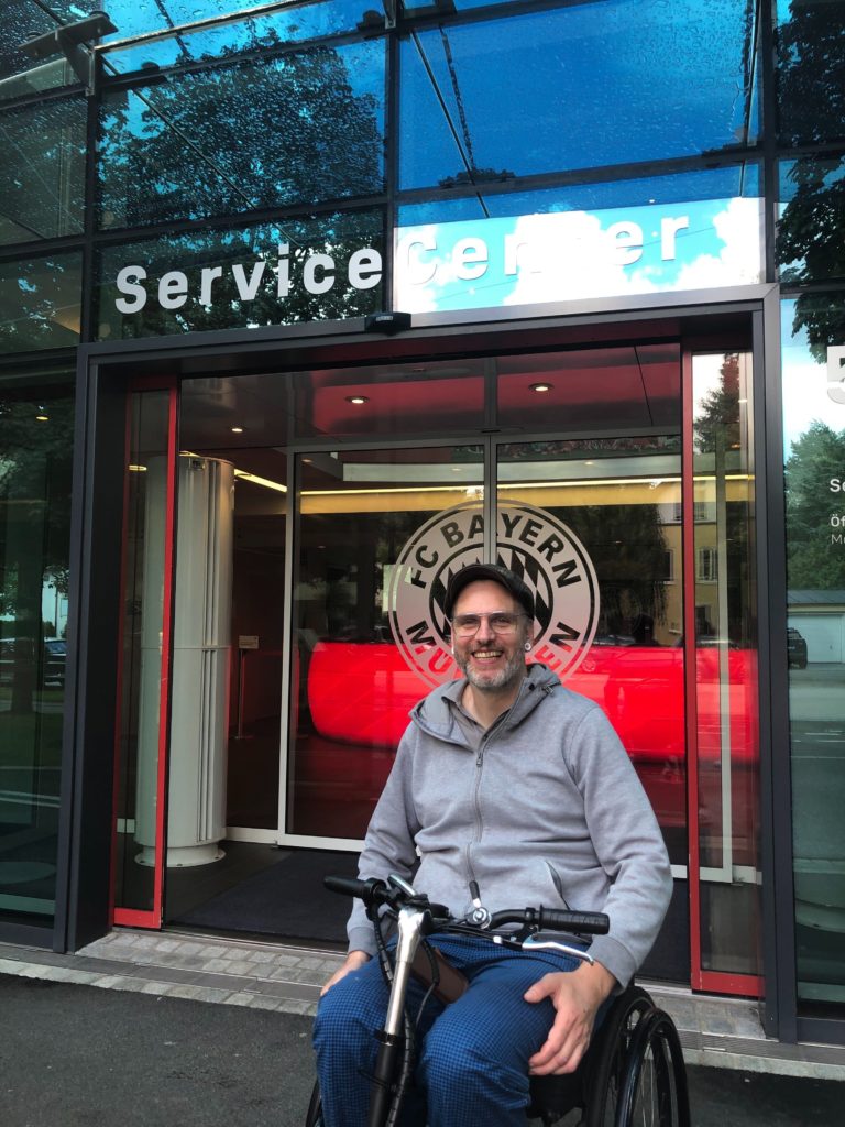 Kim Krämer im Rollstuhl vor dem FC Bayern Service Center