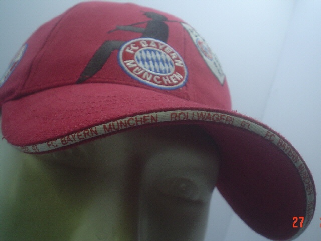 Rote Cap mit FC Bayern München Rollwagerl 93 Aufschrift am vorderen Schirmrand und Logo Rollwagerl mit FC Bayern Logo
