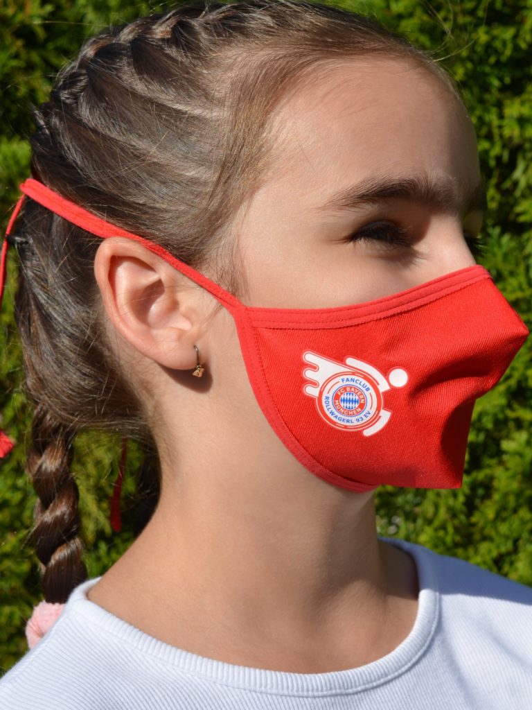 Kind mit Mund-Nasenschutz mit Rollwagerl-Logo in rot