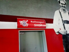 Rollwagerl-SHOP Schild in der Allianz Arena über der Tür zum SHOP. Daneben ein Bild an der Wand von Rummenigge.
