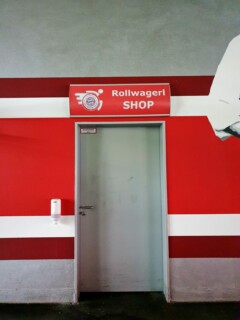 Rollwagerl-SHOP Schild bei Tag über der Tür in der Allianz Arena.
