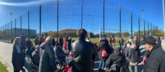 Eine Gruppe steht vor einem Fußballplatz. Der Himmel ist wolkenlos blau.