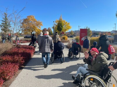 Eine Gruppe mit Rollstuhlfahrerngeht durch einen Park am Campus des FC Bayern München.