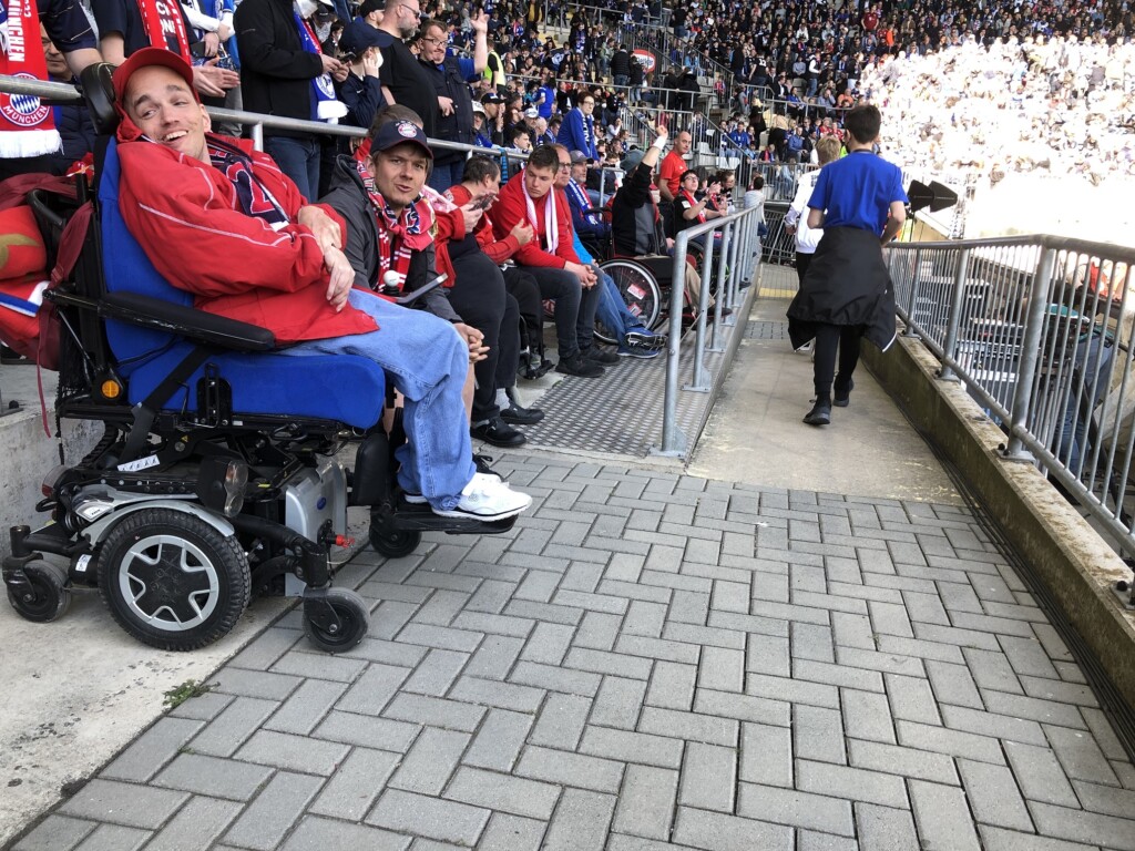 eine Reihe mit Rollstuhlfahrern vor einer Tribüne