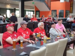 Bayern München Fans sitzen an zwei Tischen in einem Restaurant. Am Tisch im Vordergrund sitzen Rollstuhlfahrer.