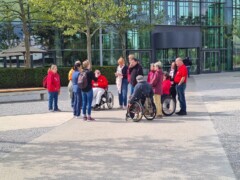 Eine Gruppe bei einer Führung auf einem Platz in der Auttadt Wolfsburg. Dabei sind auch Rollstuhlfahrer und Menschen mit Hörbehinerung und Sehbehinderung.