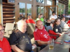 Menschen sitzen gesellig an Tischen in einem Restaurant. Es sind viele FC Bayern Fans dabei.