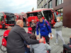 Robert Lewandowsky beim Autogramm für eine Rollstuhlfahrerin vor zwei Bussen des FC Bayern München