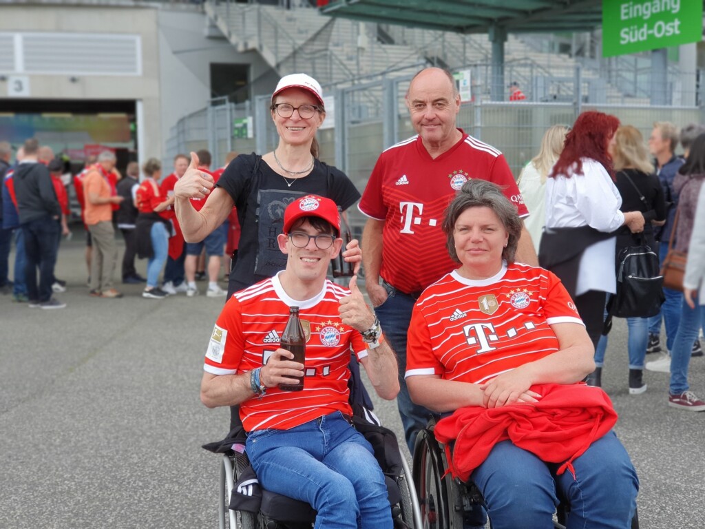 Vier Personen vor einem Stadion. Zwei davon im Rollstuhl.