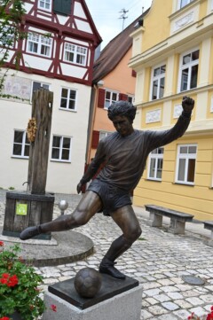 Gerd Müller Statue in Nördlingen. Im Hintergrund Fachwerkhäuser