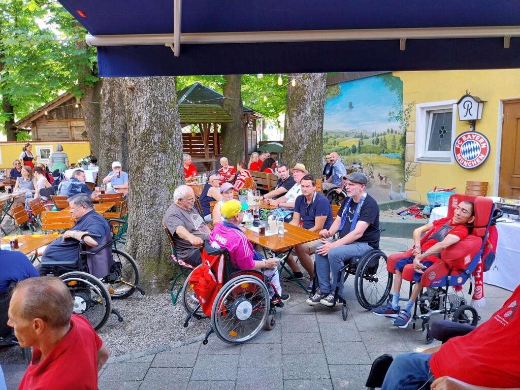 Ein Biergarten mit Fans des FC Bayern München, darunter auch viele Rollstuhlfahrer.