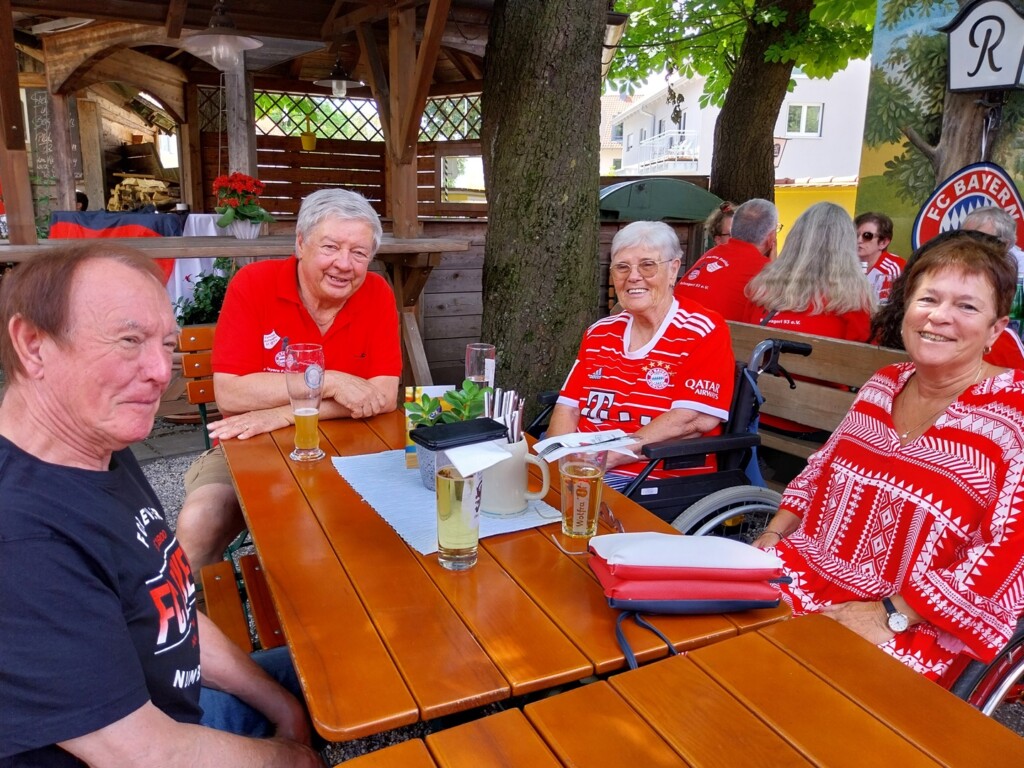 Vier FC Bayern Fans sitzen an einem Tisch in einem Biergarten.