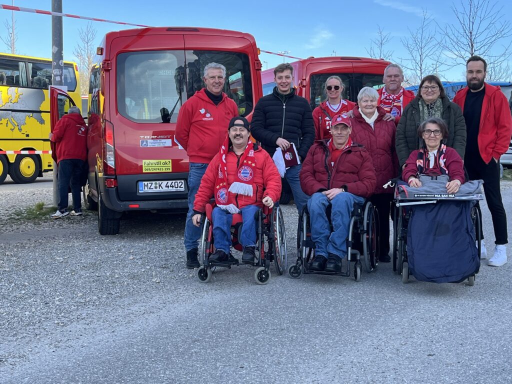 Ein Gruppenfoto von Menschen mit und ohne Rollstuhl vor zwei roten Kleinbussen