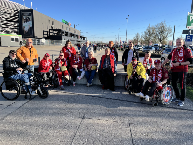 Eine Gruppenfoto mit 16 Fans des FC Bayern München vor der Arena des FC Augsburg