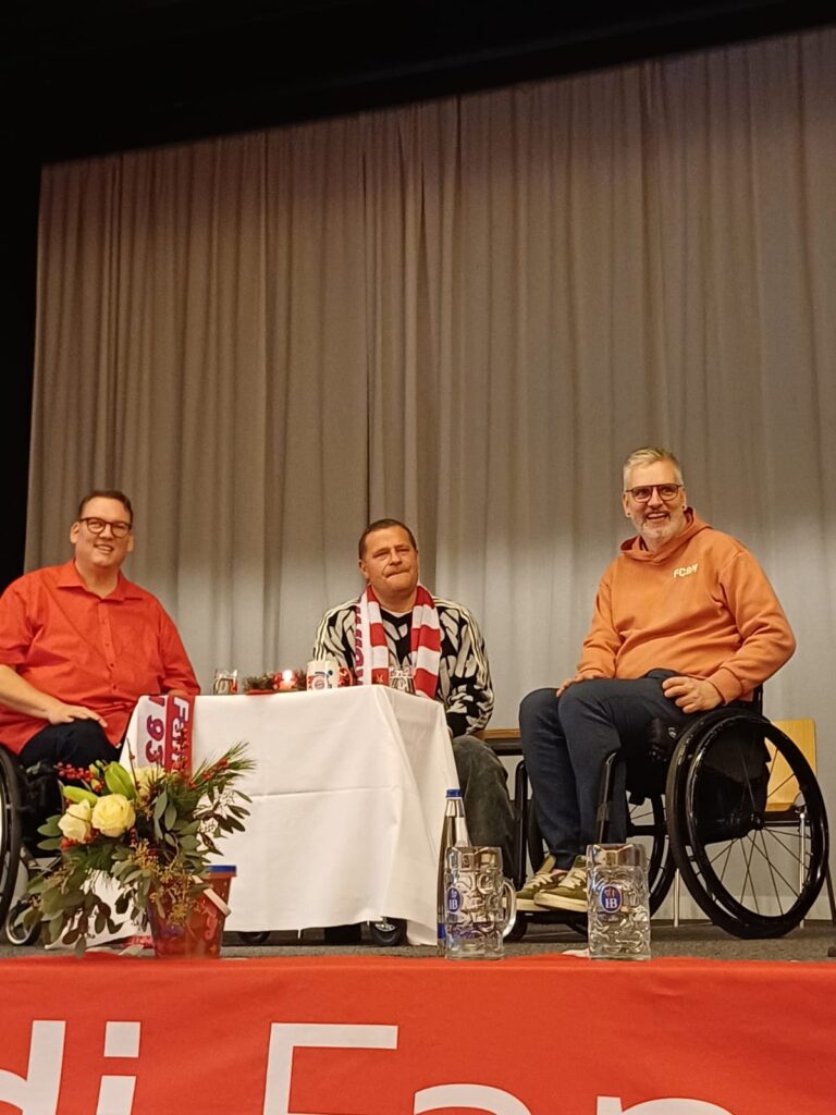 Alexander Grundler, Max Eberl und Kim Krämer sitzen auf der Bühne an einem weihnachtlich dekorierten Tisch.
